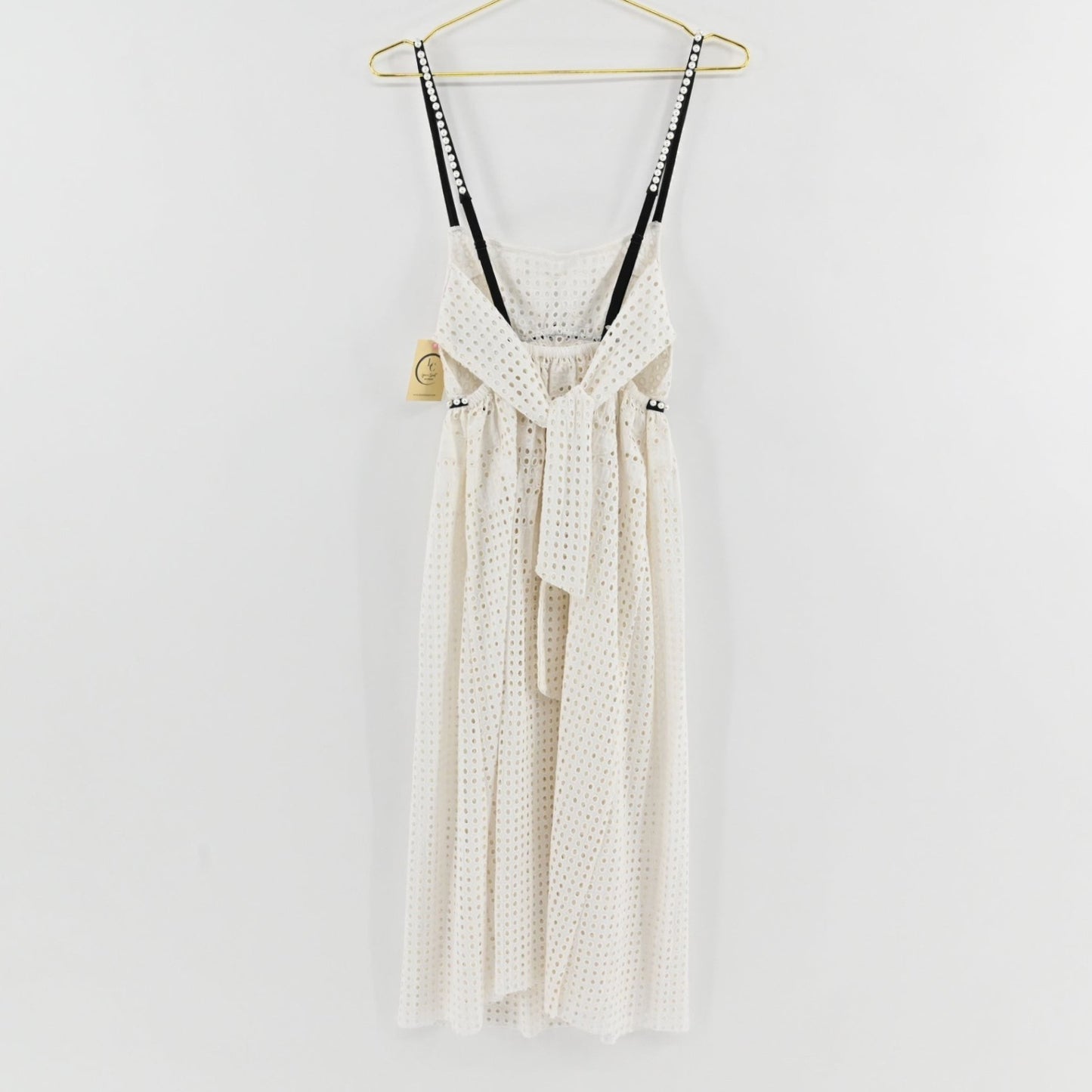 Lynn's Closet Boutique white eyelet midi dress with black pearl-embellished straps and back tie detail on a hanger.