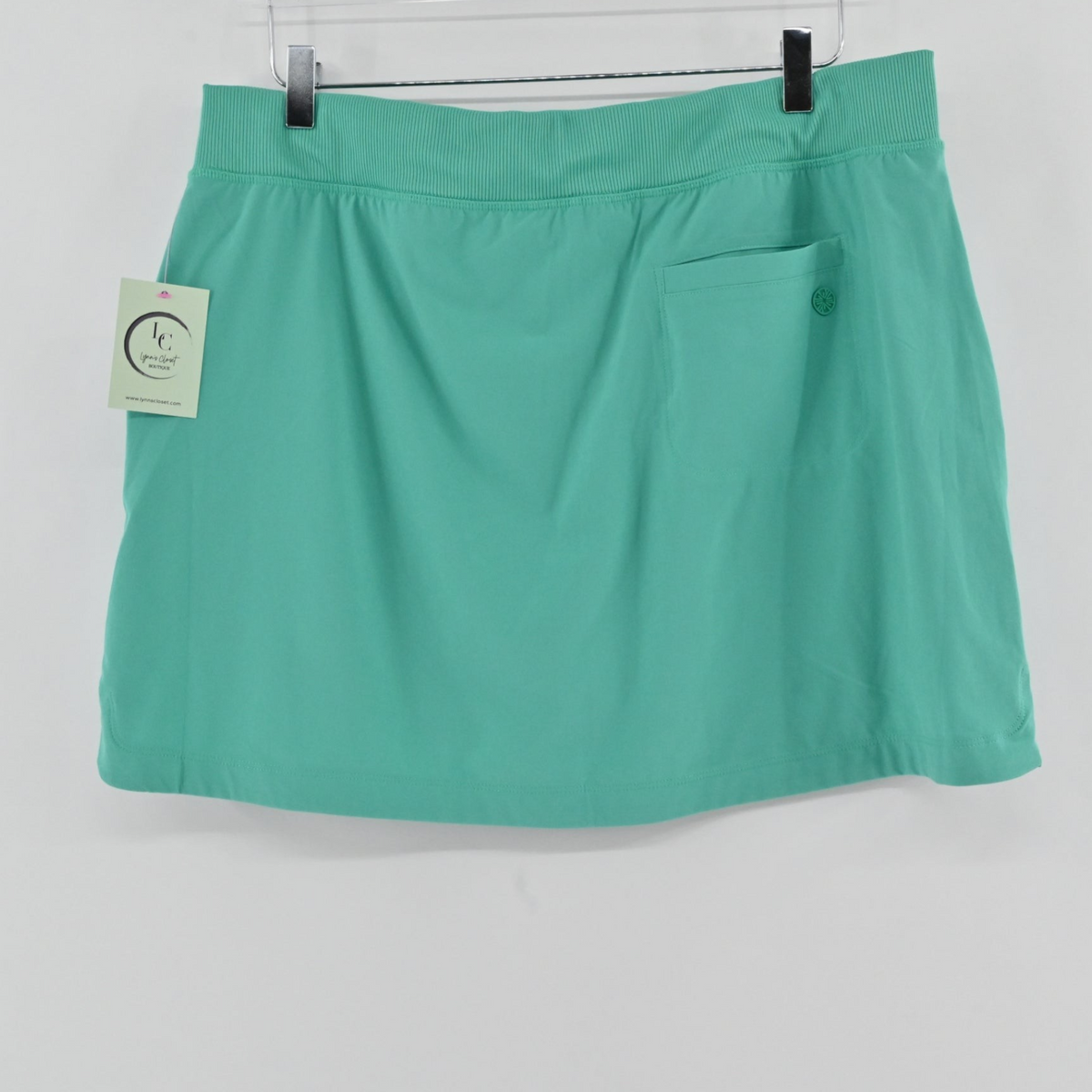 Lynn's Closet Boutique green athletic skort with a ribbed waistband and zippered back pocket hanging on a hanger.