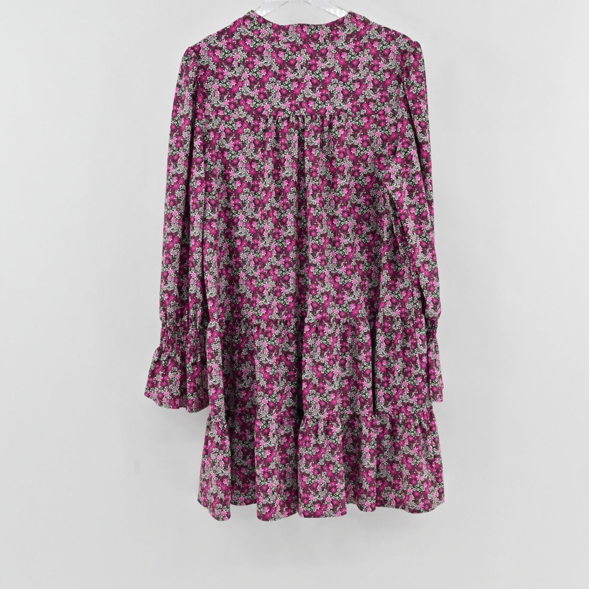 Lynn's Closet Boutique Jude Connally pink floral tiered mini dress with long sleeves and ruffled cuffs hanging on wall