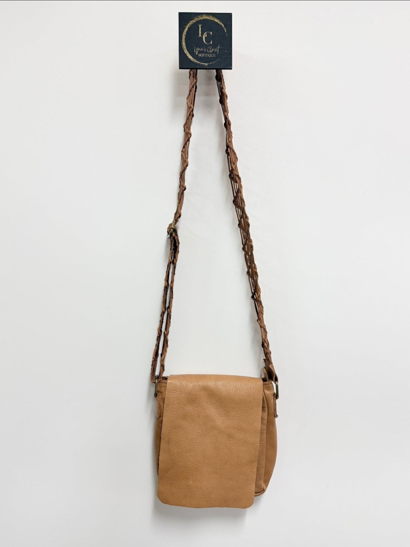 Lynn's Closet Boutique brown leather crossbody bag with a unique braided strap hanging against a white wall