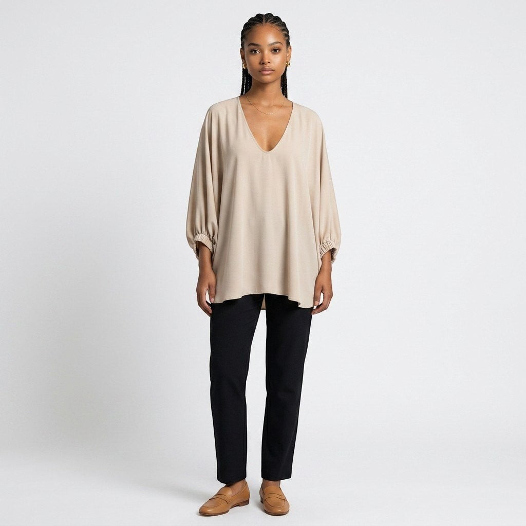 Model wearing a Lynn's Closet Boutique champagne silk V-neck top with billowy sleeves and black trousers