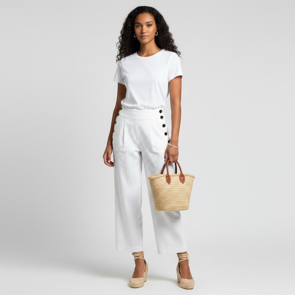 Model wearing Lynn's Closet Boutique Club Monaco white linen blend pants with side button details and a straw tote.