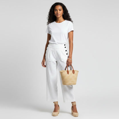 Model wearing Lynn's Closet Boutique Club Monaco white linen blend pants with side button details and a straw tote.