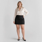 Model wearing a Lynn's Closet Boutique Good American black mini skirt with a cream satin blouse and black heels
