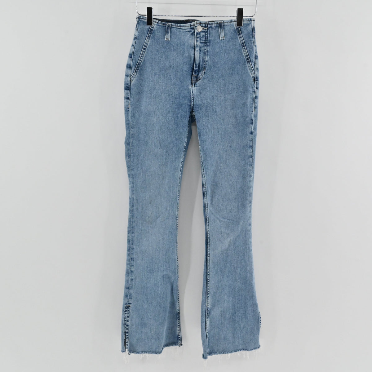 Lynn's Closet Boutique We The Free light wash high-rise flare jeans with a raw split hem hanging on a hanger.