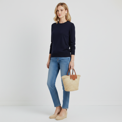 Model wearing a Lynn's Closet Boutique navy blue crew neck sweater with blue jeans, espadrilles, and a straw bag.