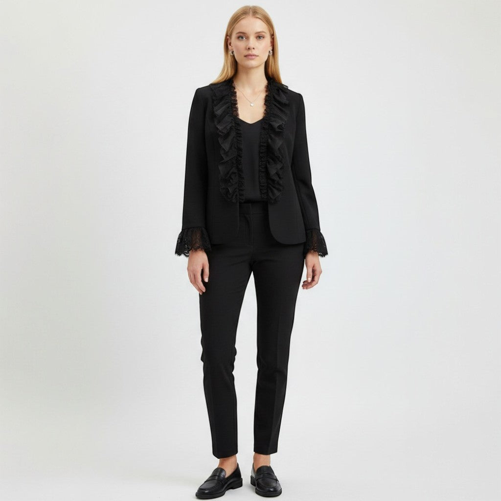 Model wearing a black Nina Raynor ruffle lace jacket with matching trousers and loafers against a white background.