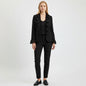 Model wearing a black Nina Raynor ruffle lace jacket with matching trousers and loafers against a white background.