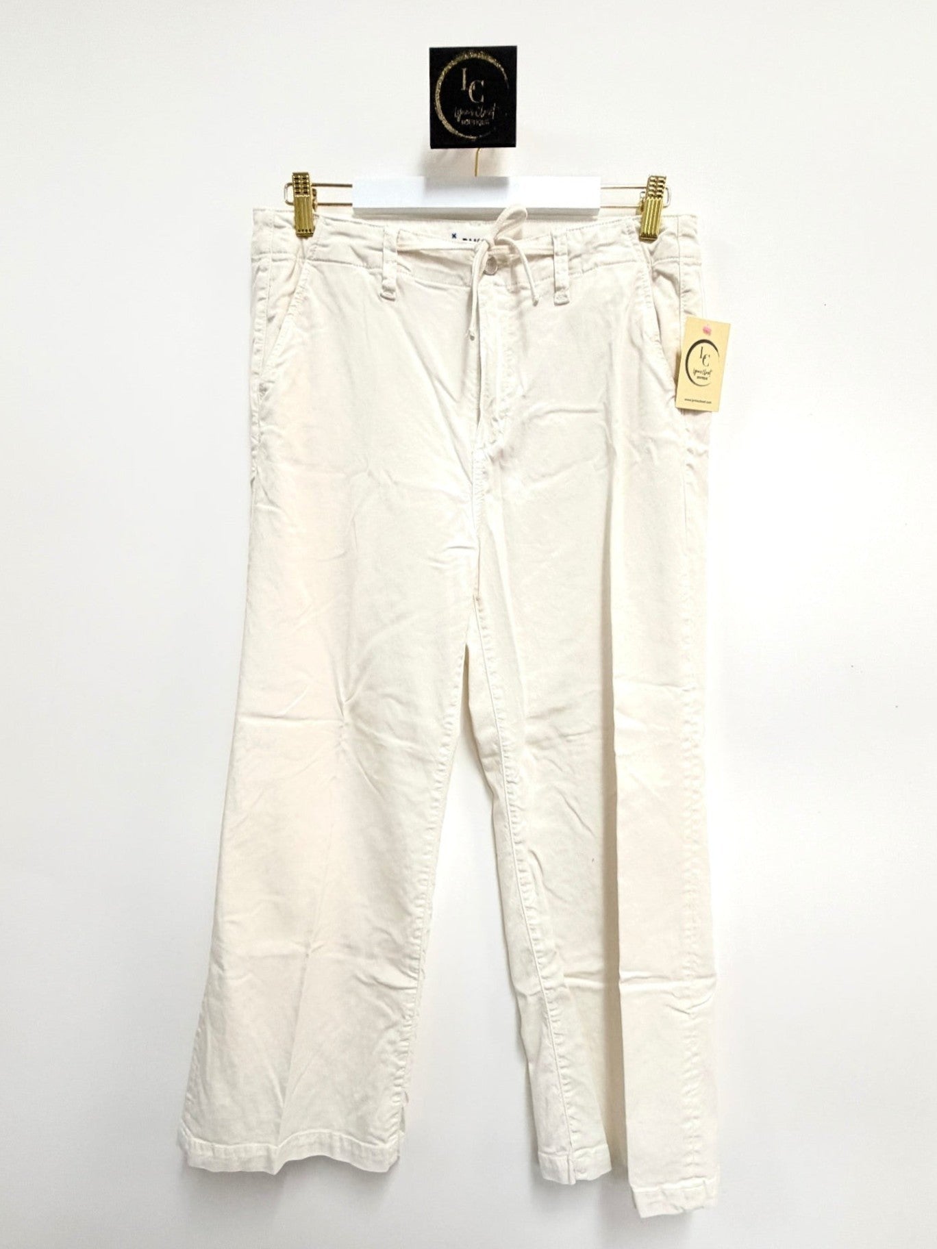 Lynn's Closet Boutique Paige white wide-leg pants with a drawstring waist and pockets hanging against a white wall.