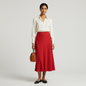 Model wearing a red Karen Kane bias-cut midi skirt with a white blouse, pearl necklace, and brown handbag.