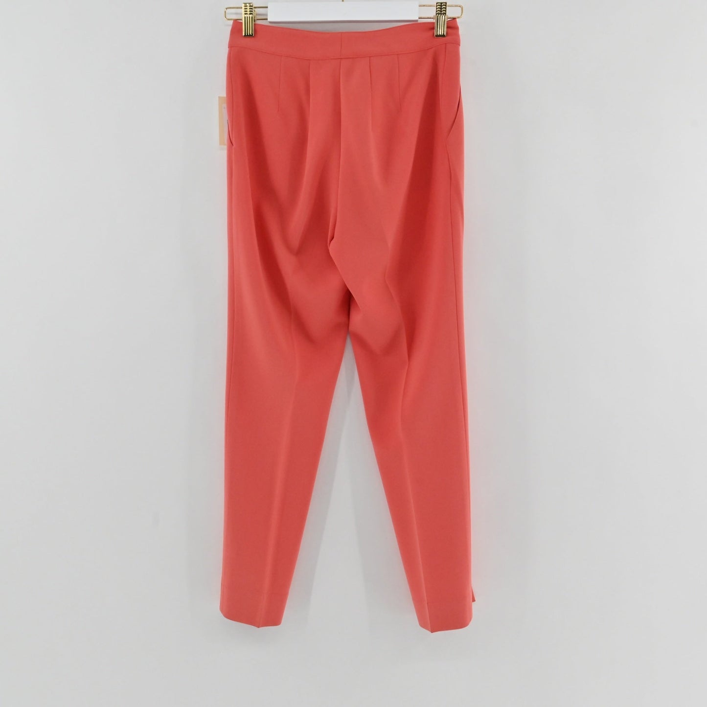 Lynn's Closet Boutique St. John coral slim-leg trousers hanging on a hanger, featuring a clean waistband and creases.