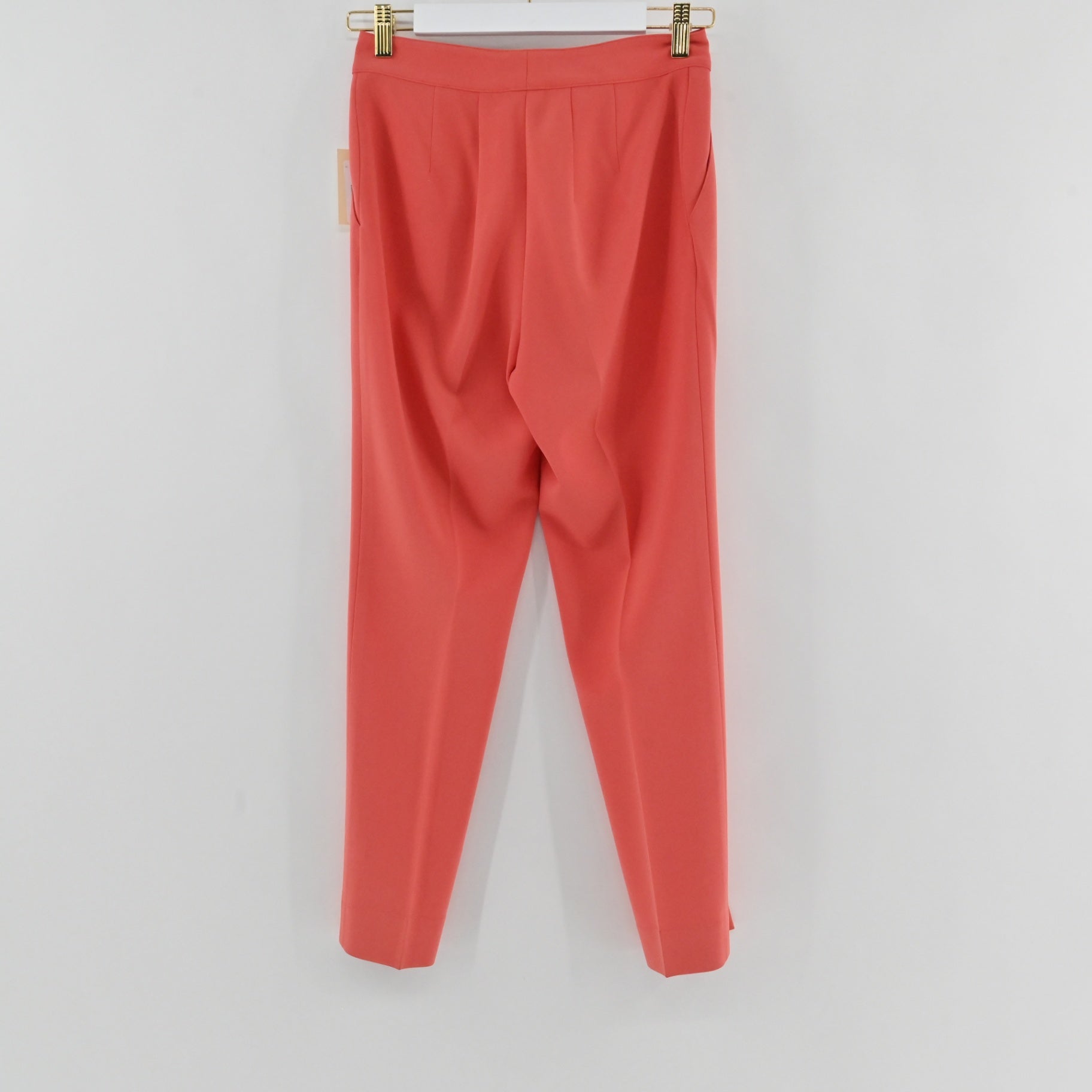 Lynn's Closet Boutique St. John coral slim-leg trousers hanging on a hanger, featuring a clean waistband and creases.