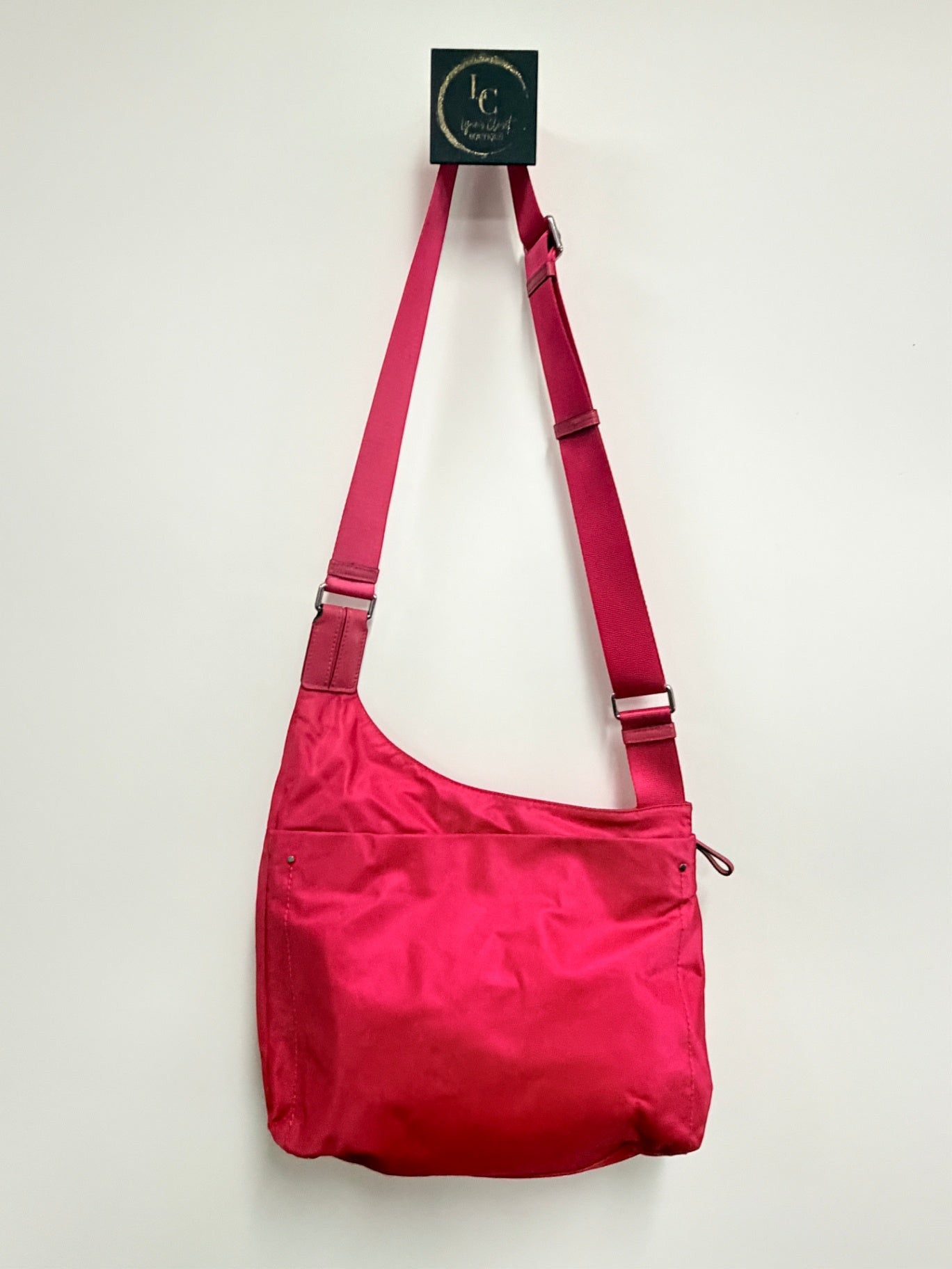 Lynn's Closet Boutique Tumi Voyageur hot pink nylon crossbody bag with an adjustable shoulder strap hanging on a wall.