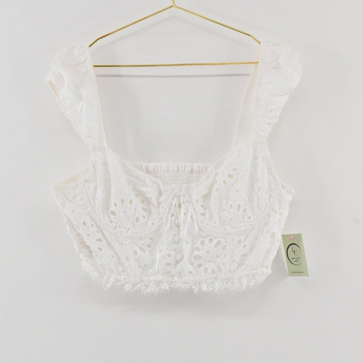 Lynn's Closet Boutique white eyelet cropped corset top with ruffled straps and a smocked back on a gold hanger.