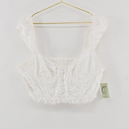 Lynn's Closet Boutique white eyelet cropped corset top with ruffled straps and a smocked back on a gold hanger.