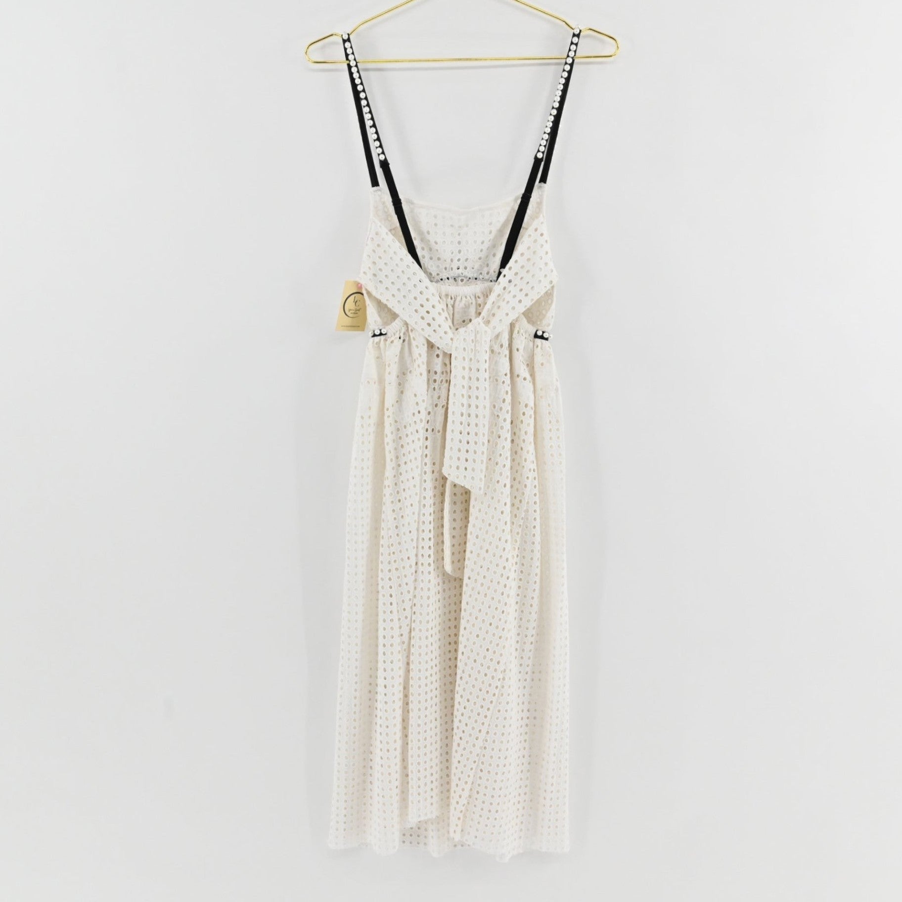 Lynn's Closet Boutique white eyelet midi dress with black pearl-embellished straps and back tie detail on a hanger.
