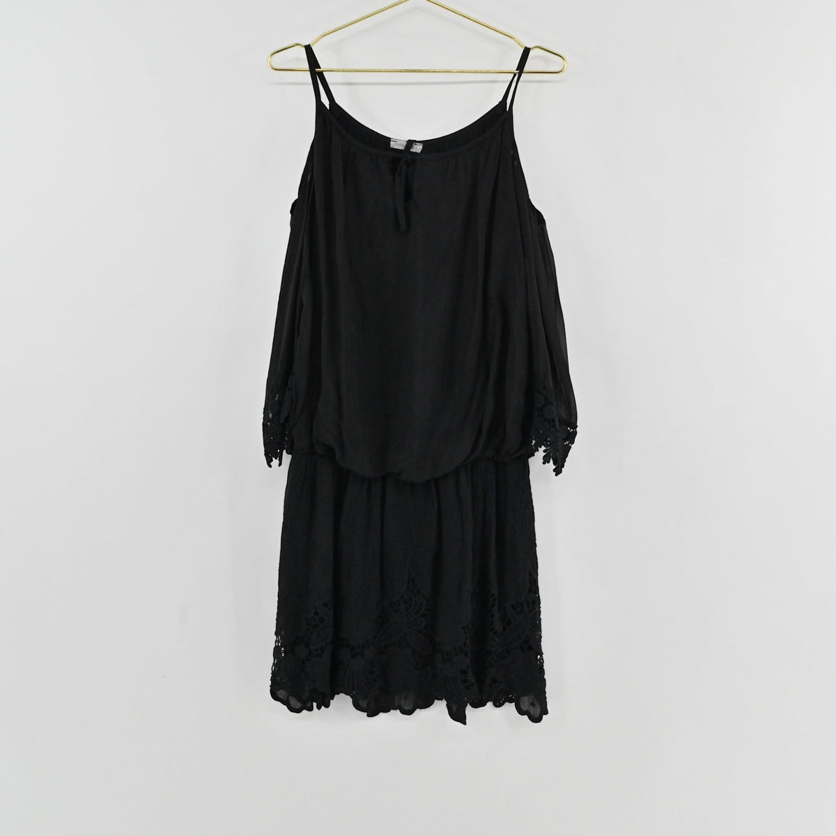 Lynn's Closet Boutique black cold-shoulder dress with lace trim and spaghetti straps hanging on a gold hanger