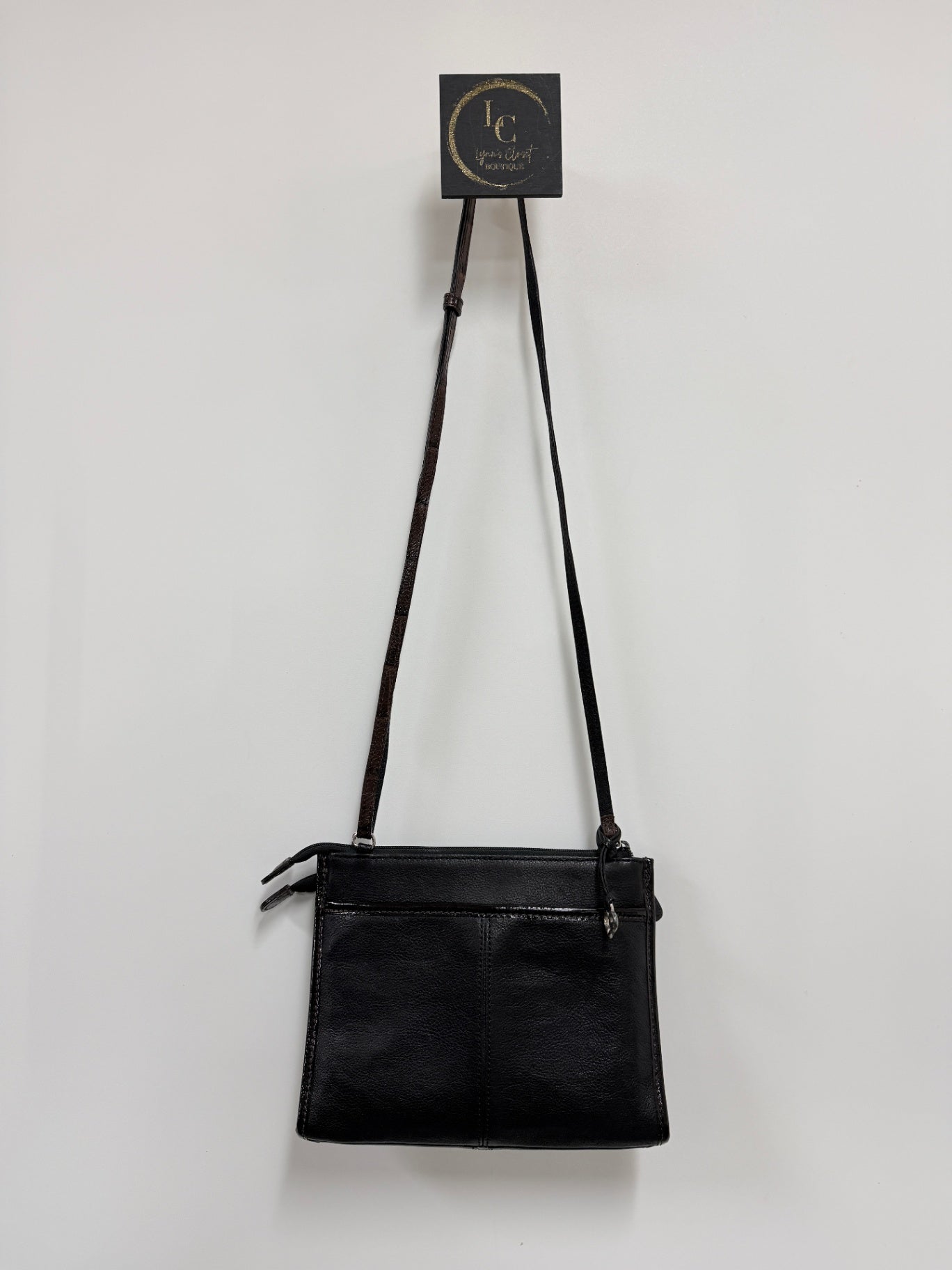 Lynn's Closet Boutique Brighton crossbody bag in black with brown strap and silver hardware hanging on a wall