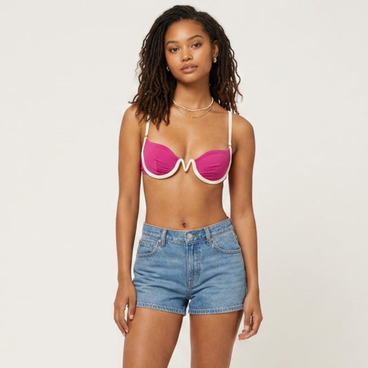 Model wearing a Lynn's Closet Boutique L Space fuchsia bikini top with white trim and denim shorts