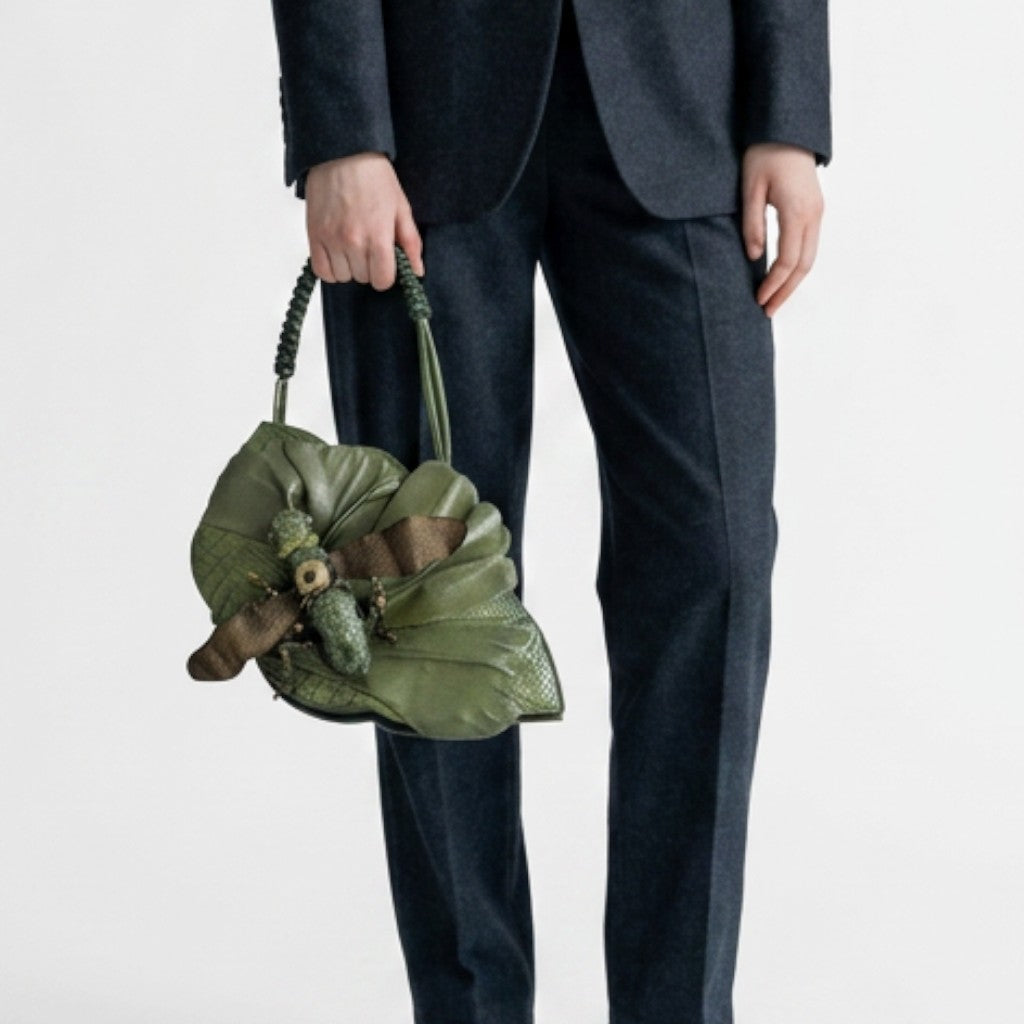 Lynn's Closet Boutique green leather grasshopper-shaped handbag with braided strap held by a person in a dark suit.