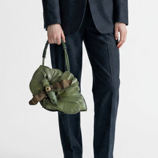 Lynn's Closet Boutique green leather grasshopper-shaped handbag with braided strap held by a person in a dark suit.