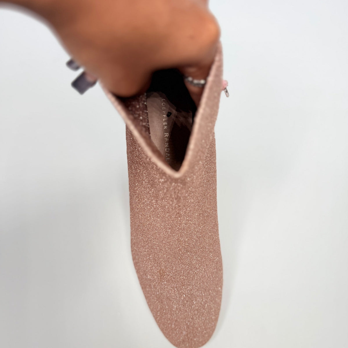 Lynn's Closet Boutique Loeffler Randall Carter ankle booties in rose gold glitter held by hand showing interior label