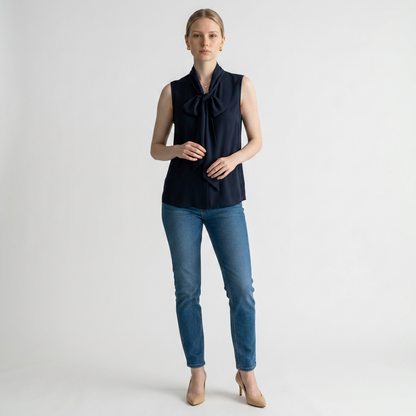 Model wearing a Lynn's Closet Boutique navy sleeveless Tory Burch top with a tie-neck bow and blue jeans.