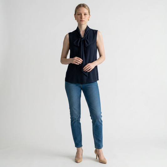 Model wearing a Lynn's Closet Boutique navy sleeveless Tory Burch top with a tie-neck bow and blue jeans.