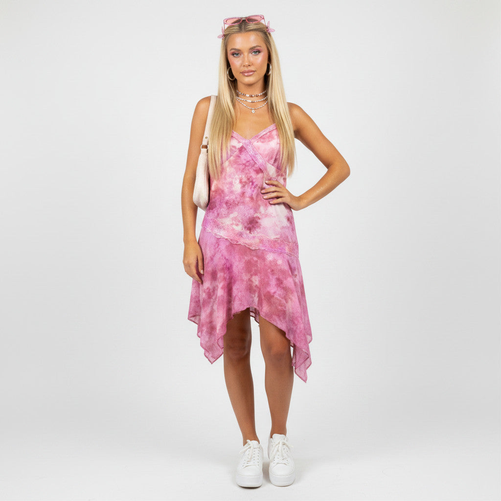 Model wearing a Lynn's Closet Boutique pink tie-dye asymmetrical dress with lace trim and white sneakers