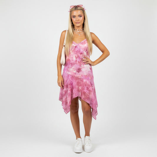 Model wearing a Lynn's Closet Boutique pink tie-dye asymmetrical dress with lace trim and white sneakers