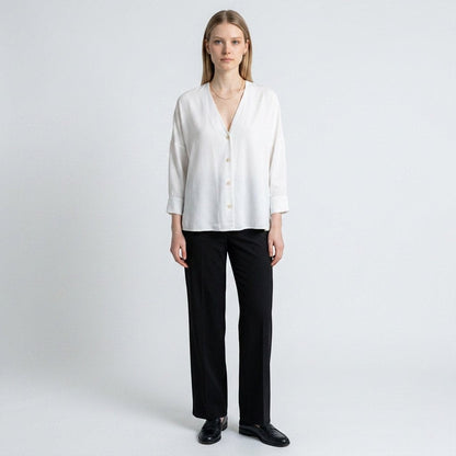 A model wearing a white Sandro button-down top with a V-neckline, paired with black trousers from Lynn's Closet Boutique.
