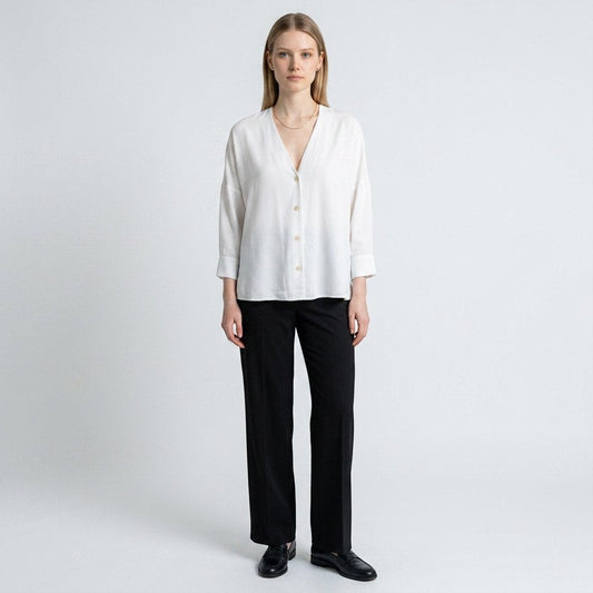 A model wearing a white Sandro button-down top with a V-neckline, paired with black trousers from Lynn's Closet Boutique.