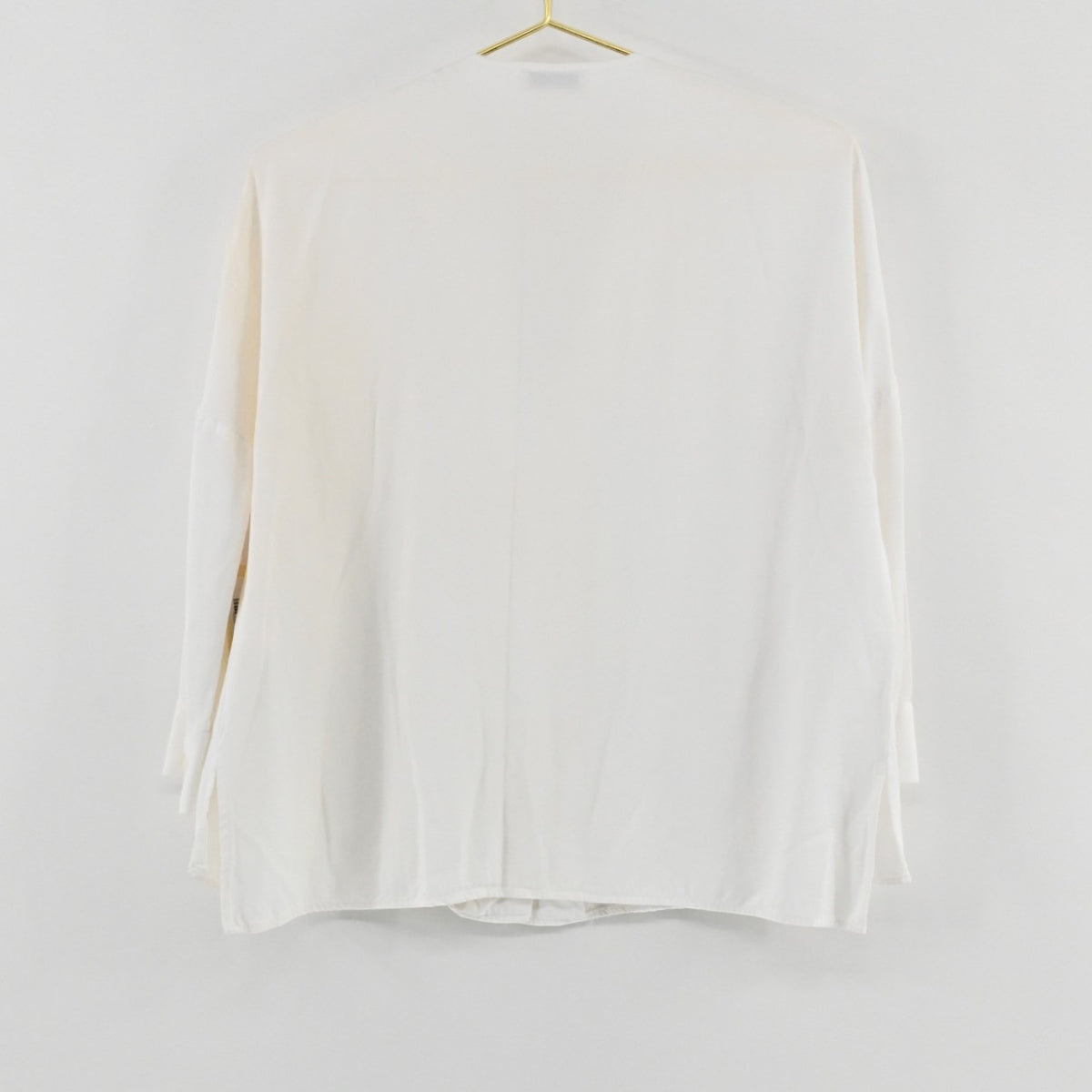 Lynn's Closet Boutique Sandro white long-sleeve top hanging on a gold hanger, back view showing a relaxed silhouette.