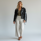 Model wearing a Lynn's Closet Boutique vintage black leather jacket with fringe, olive top, and beige wide-leg pants.