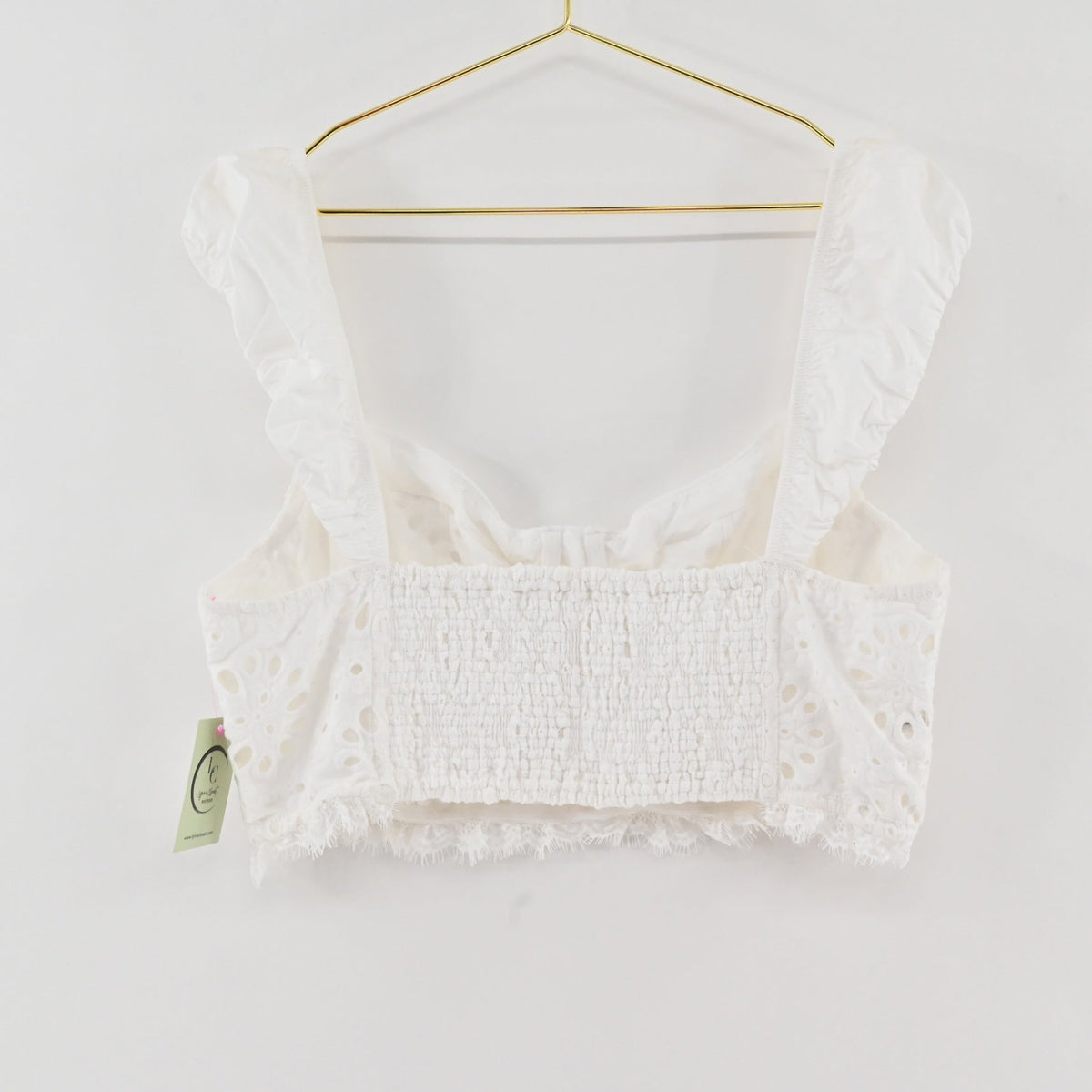 Lynn's Closet Boutique white eyelet cropped corset top with ruffled straps and smocked back on a gold hanger