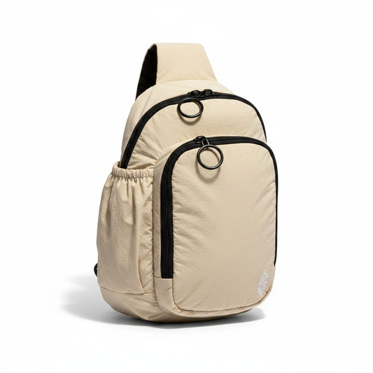 Free People tan nylon sling bag with black zippers and drawstring side pocket. Features embroidered logo.
